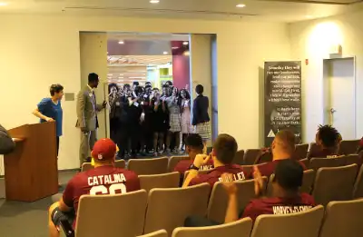 students stand while football players sit
